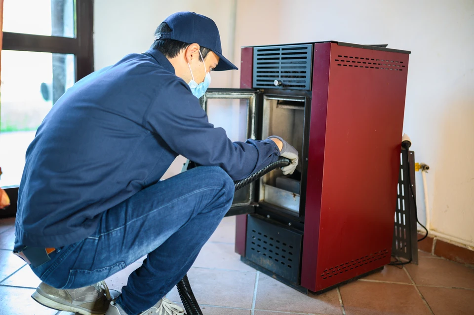 Un technicien en uniforme bleu et casquette effectue la maintenance d'un appareil de chauffage domestique rouge bordeaux