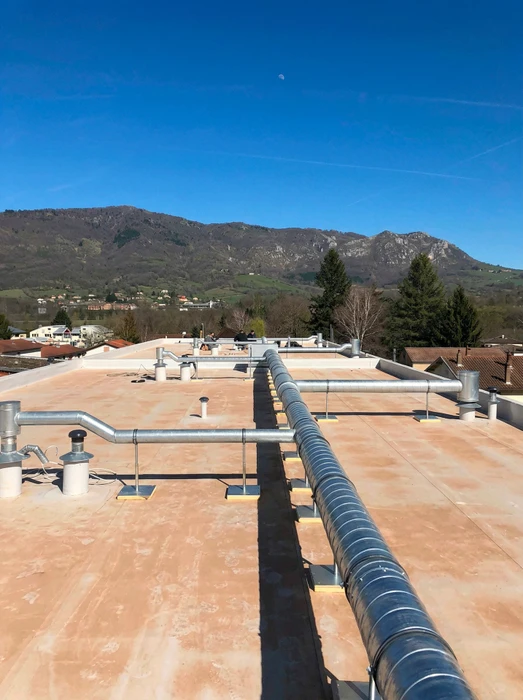Toiture-terrasse commerciale avec réseau de gaines de ventilation en acier galvanisé, dont une gaine flexible spiralée de grand diamètre (~300mm)