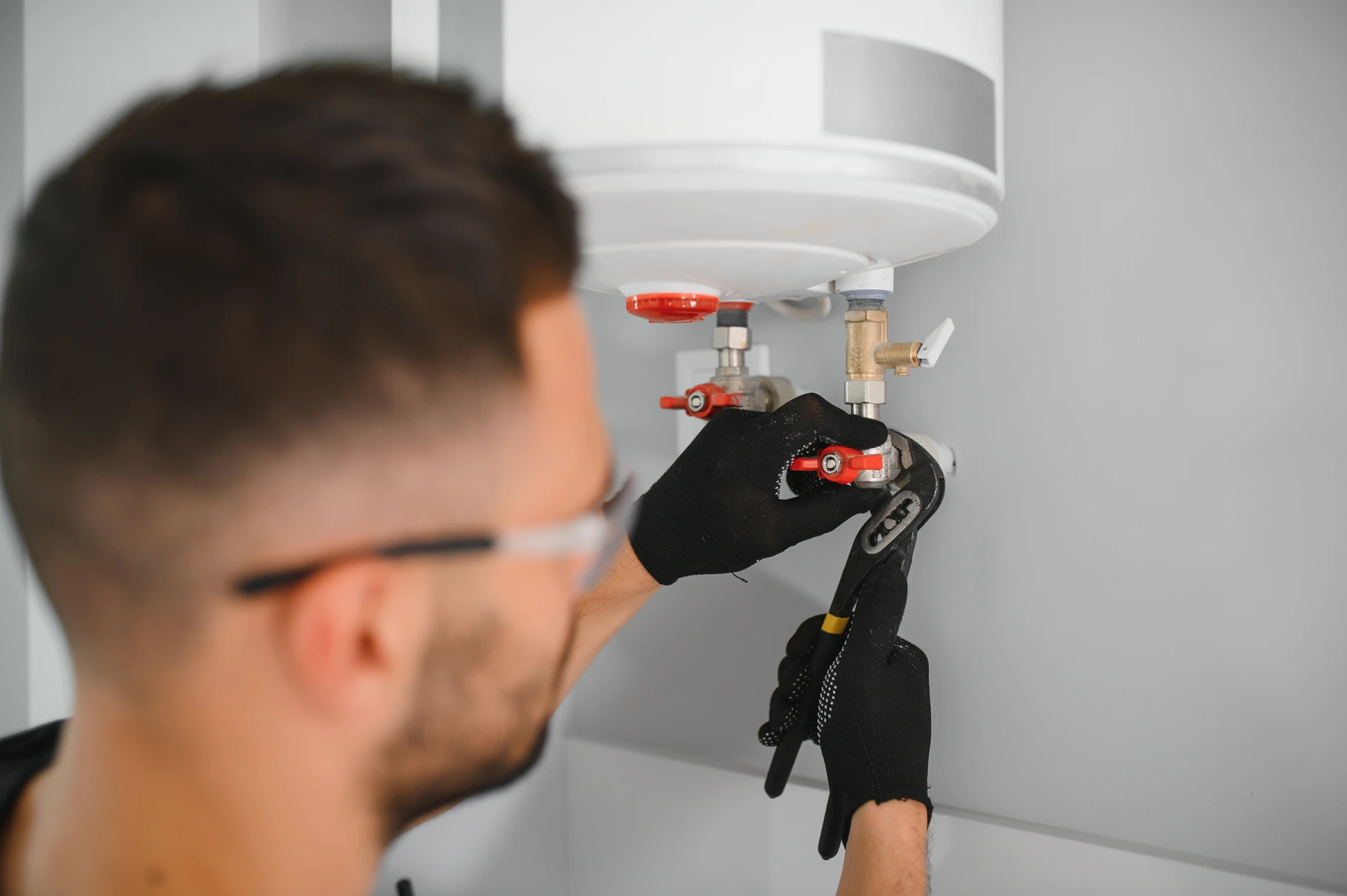 Main gauche masculine ajustant le thermostat d'un chauffe-eau électrique mural blanc dans salle de bains carrelée